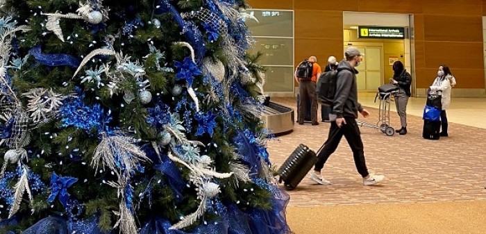 Des voyageurs au carrousel à bagages à côté des arbres de Noël exposés à l'intérieur de l'aérogare.