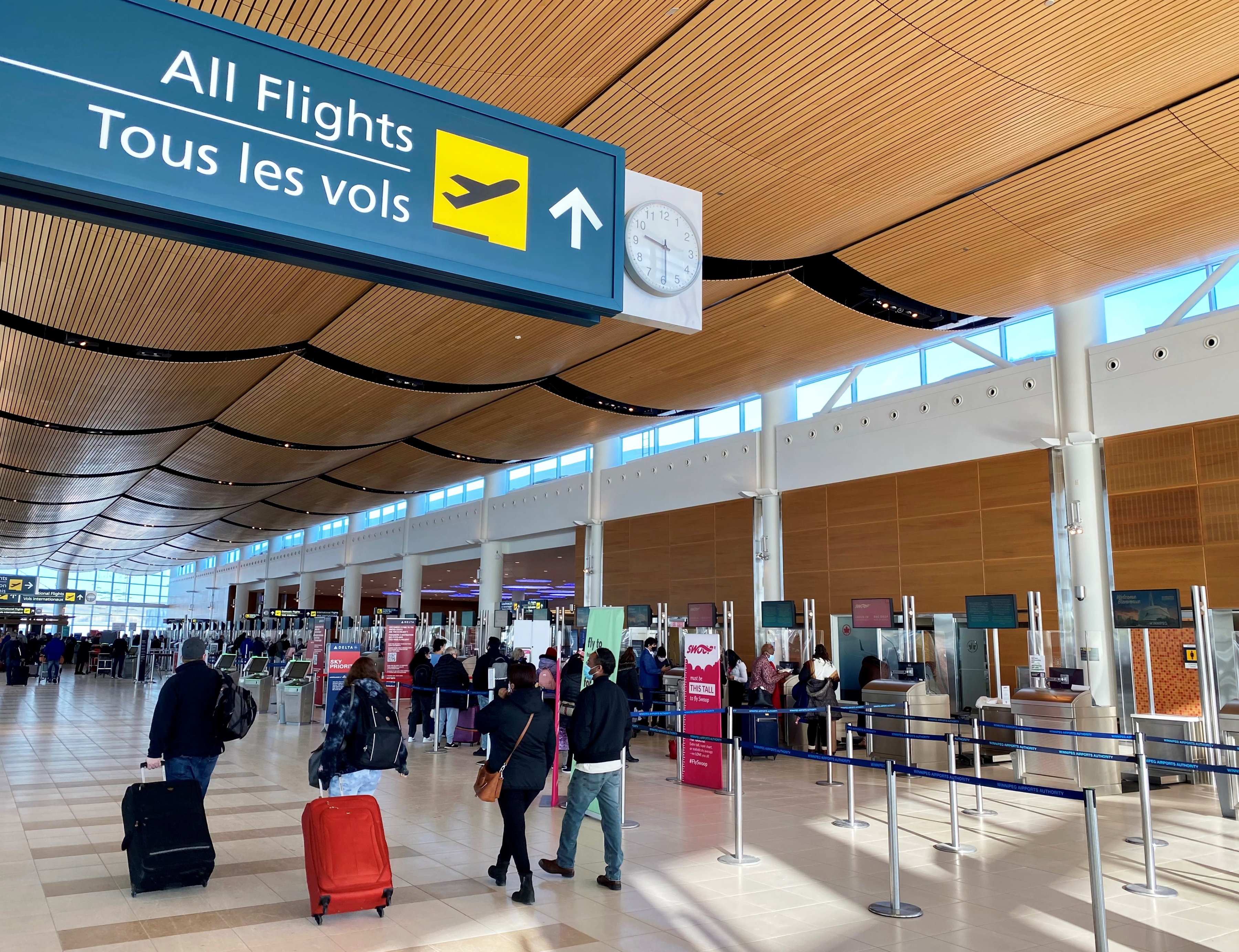 Des voyageurs passent près d'un panneau indiquant « Tous les vols » au niveau des départs de l'aérogare de l'aéroport international Richardson de Winnipeg.