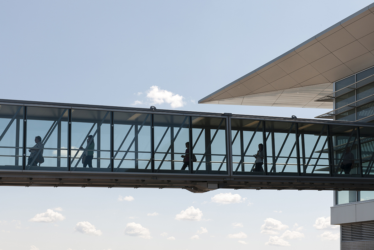 From a photo taken outside, silhouetted travellers are shown through glass walls walking down a boarding bridge away from the Winnipeg Richardson International Airport terminal.