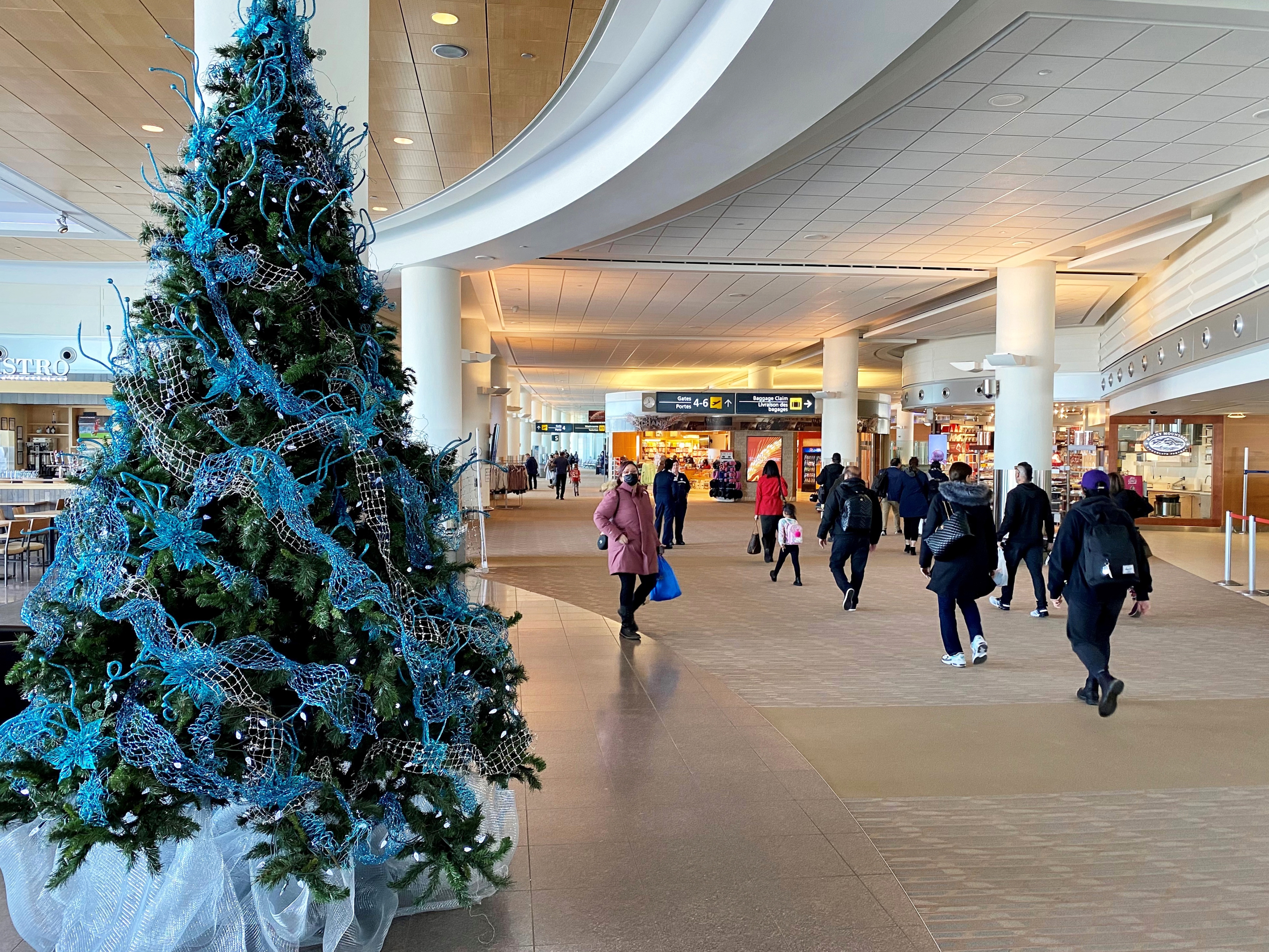 Des voyageurs passent devant un arbre décoré pour les Fêtes dans la zone des portes d'embarquement des vols intérieurs et internationaux de l'aéroport international Richardson de Winnipeg.