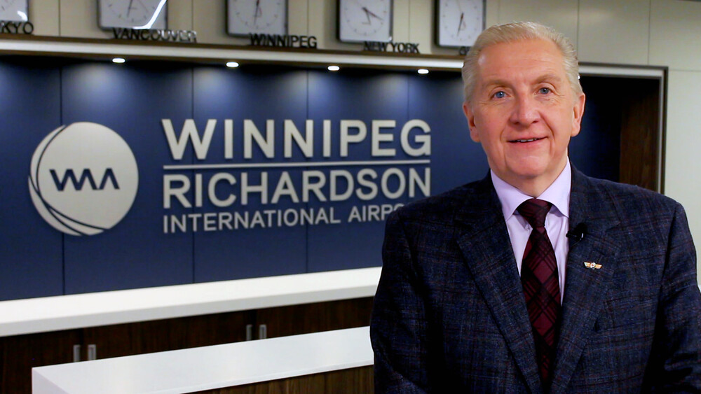 WAA President and CEO Barry Rempel poses in front of a Winnipeg Richardson International Airport sign.