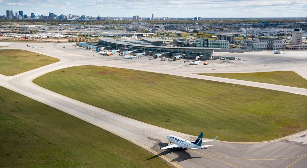 Un avion de WestJet se dirige vers l'aérogare de l'aéroport international Richardson de Winnipeg, avec l'horizon de la ville en arrière-plan.