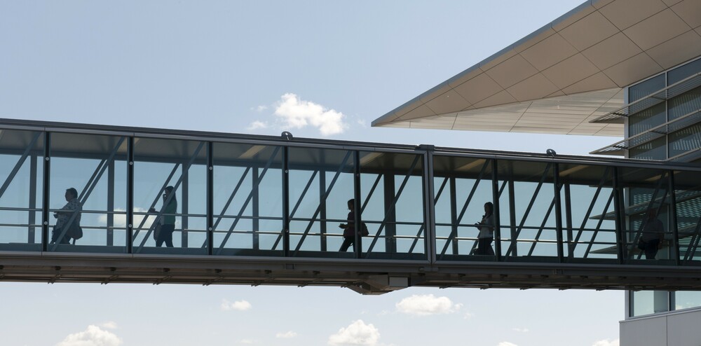 In a picture taken outside, travellers are shown walking away from the terminal and down one of the glass-walled boarding bridges at Winnipeg Richardson International Airport.