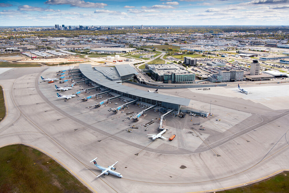 A plane pulls away from the Winnipeg Richardson International Airport terminal with the Winnipeg skyline in the distance.